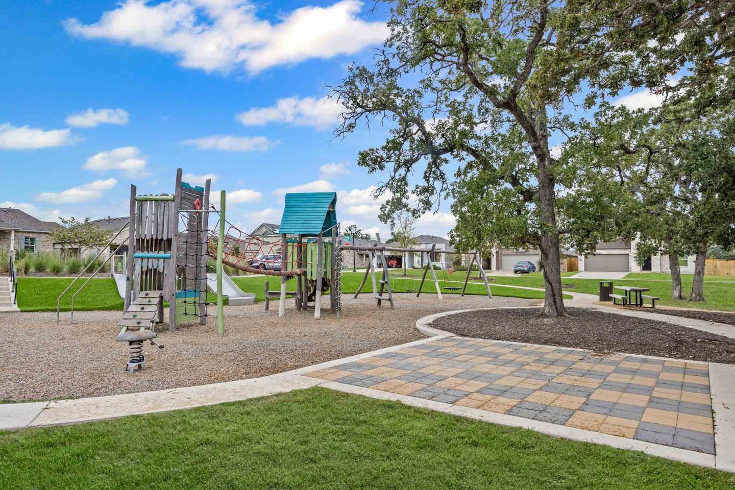 Community play area in Bastrop with climbing equipment, benches and mature trees