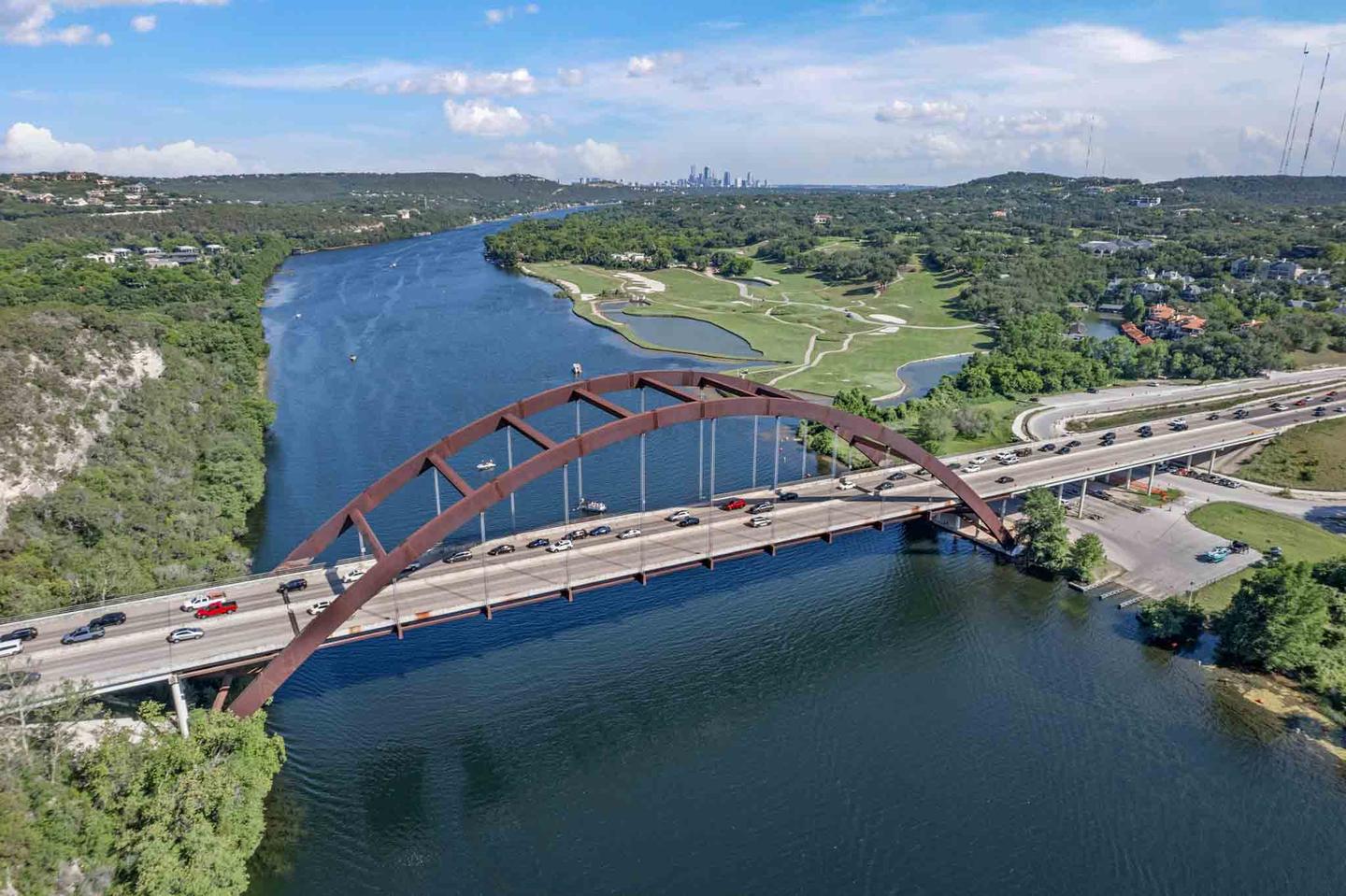 Aerial view of the Pennybacker Bridge arching over Lake Austin with hill country on both banks