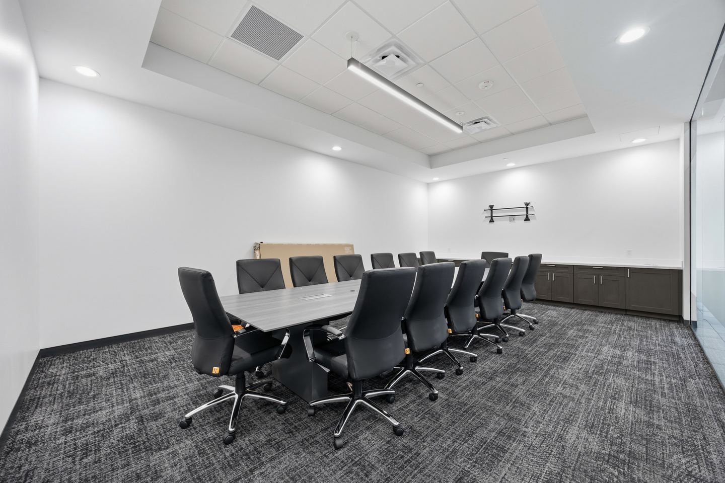 Office conference room with a long gray table, black high back chairs and patterned carpet