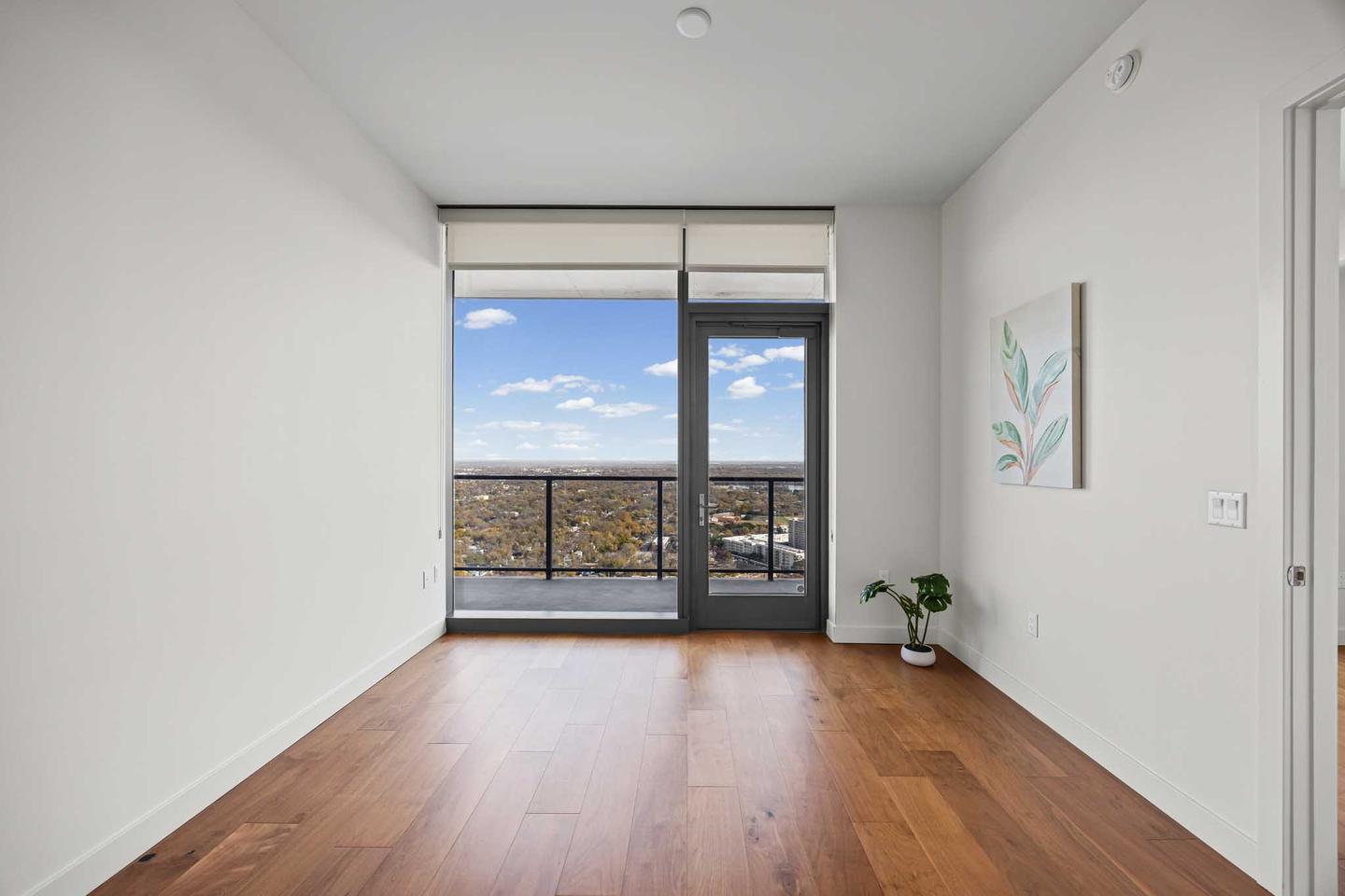 Empty downtown condo living room with bare wood floors and a wall of glass