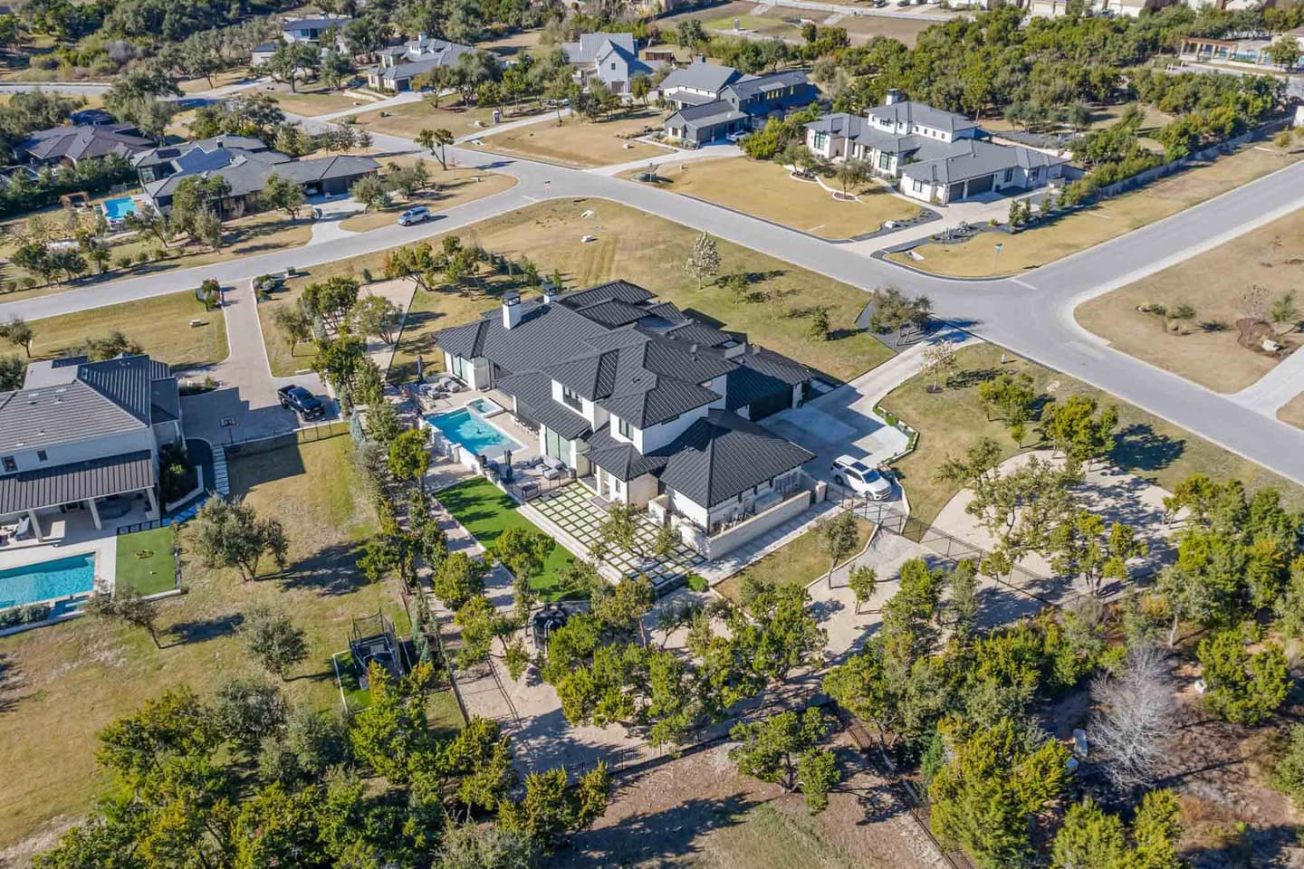 Aerial drone view of a Westlake home with a pool, mature trees and the surrounding neighborhood