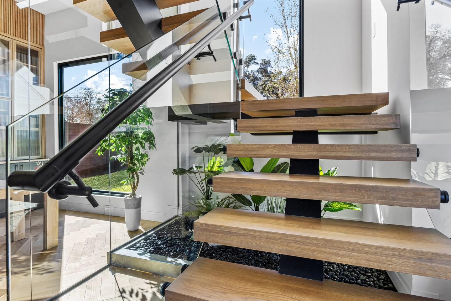 Close view of an open tread timber staircase and its steel handrail against a white wall