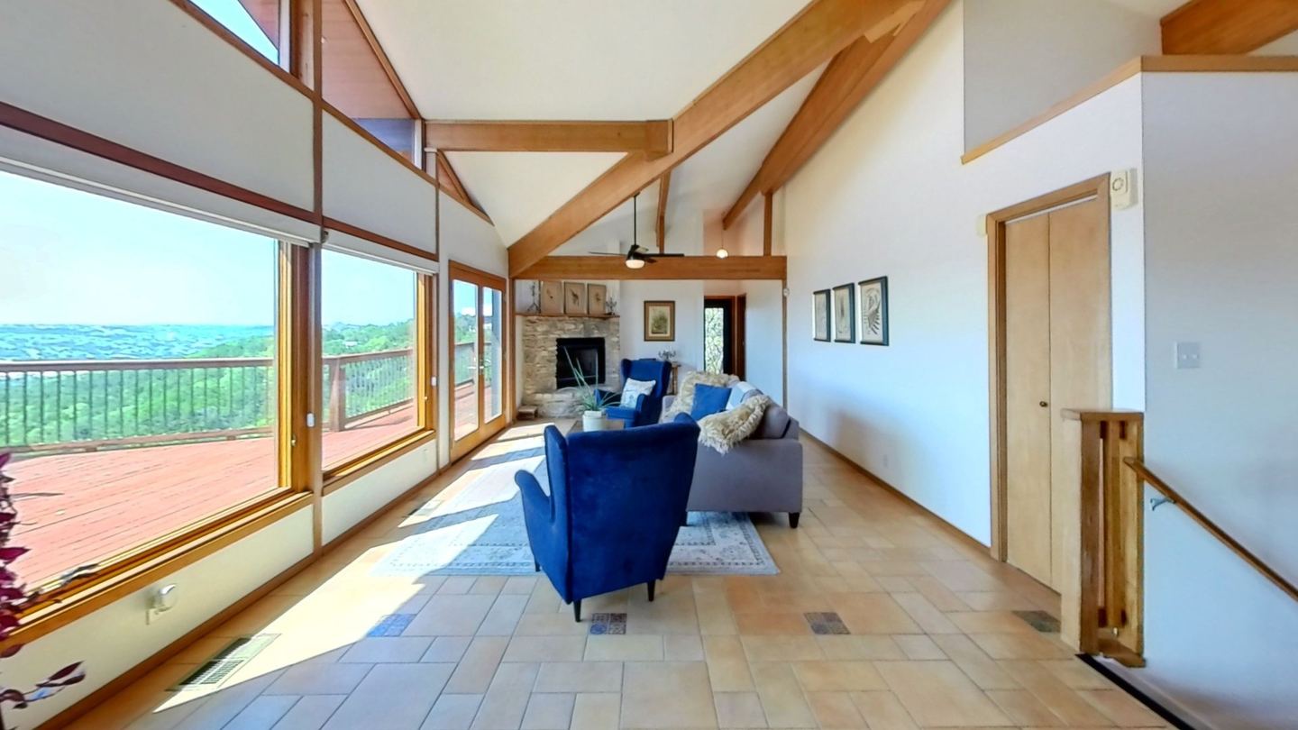 Matterport tour view of a vaulted great room with timber beams and a wall of windows onto a hill country view