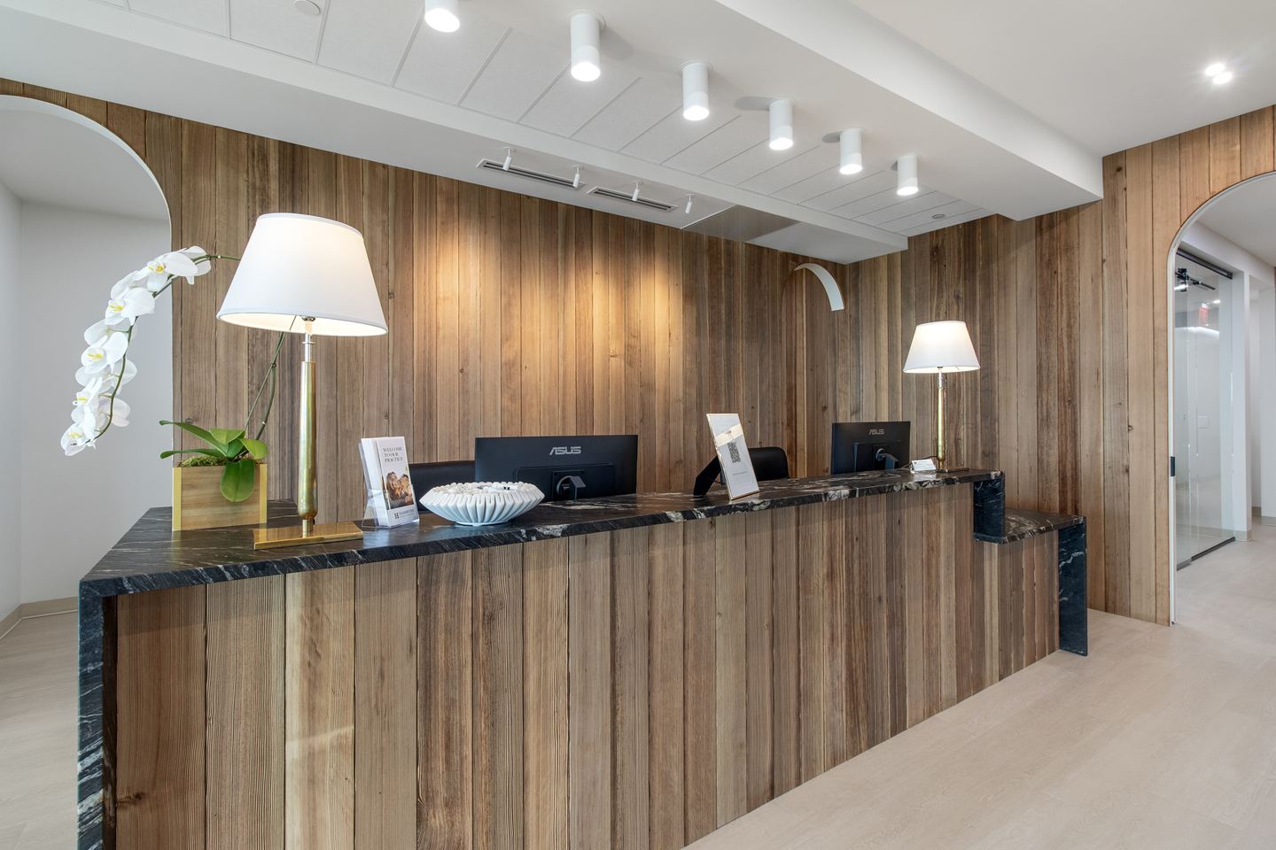 Dental office reception desk in reclaimed timber with a black stone counter, brass lamps and an orchid