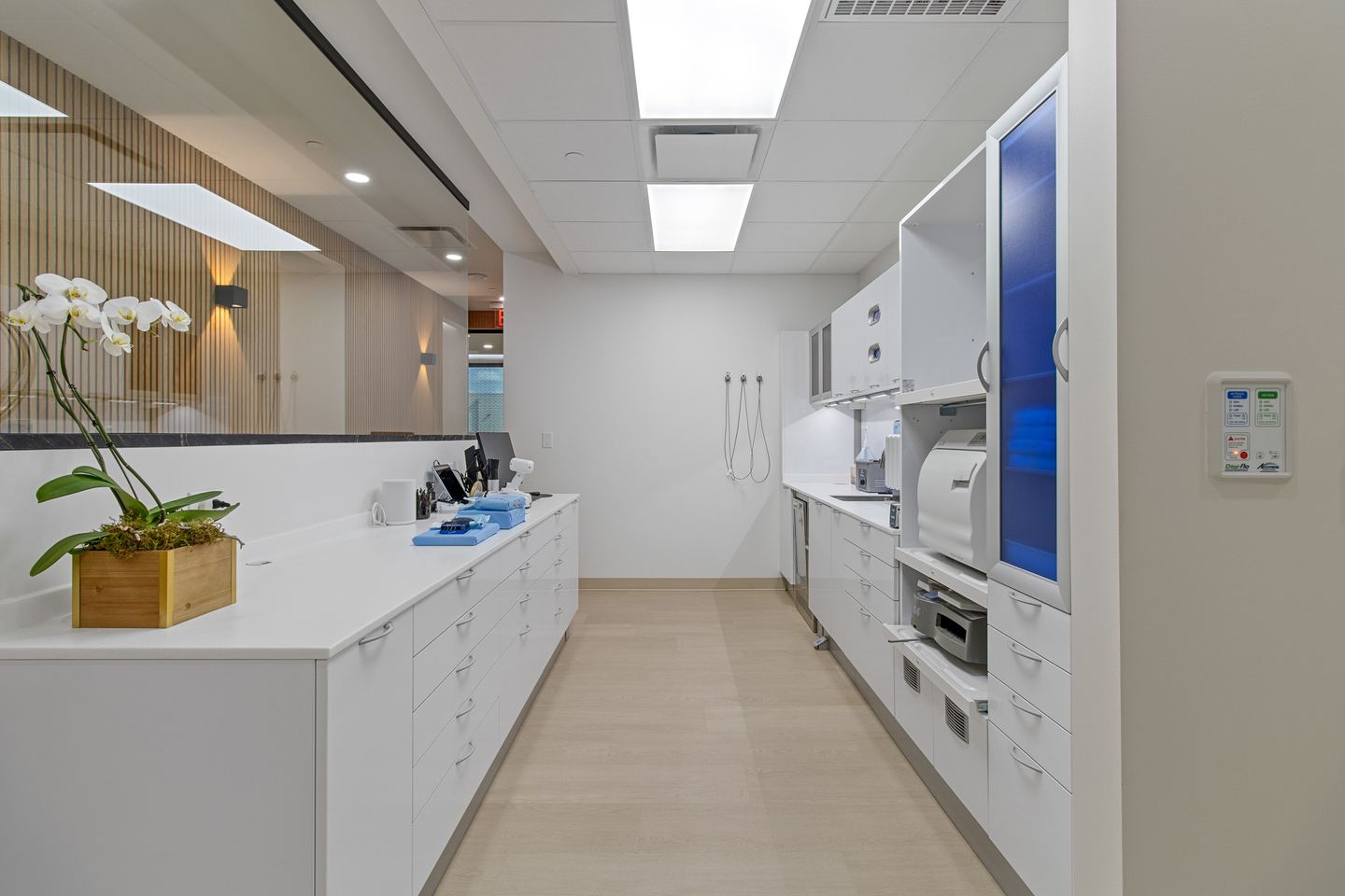 Long sterilization bay in white cabinetry with an orchid on the counter and a timber slat wall beyond