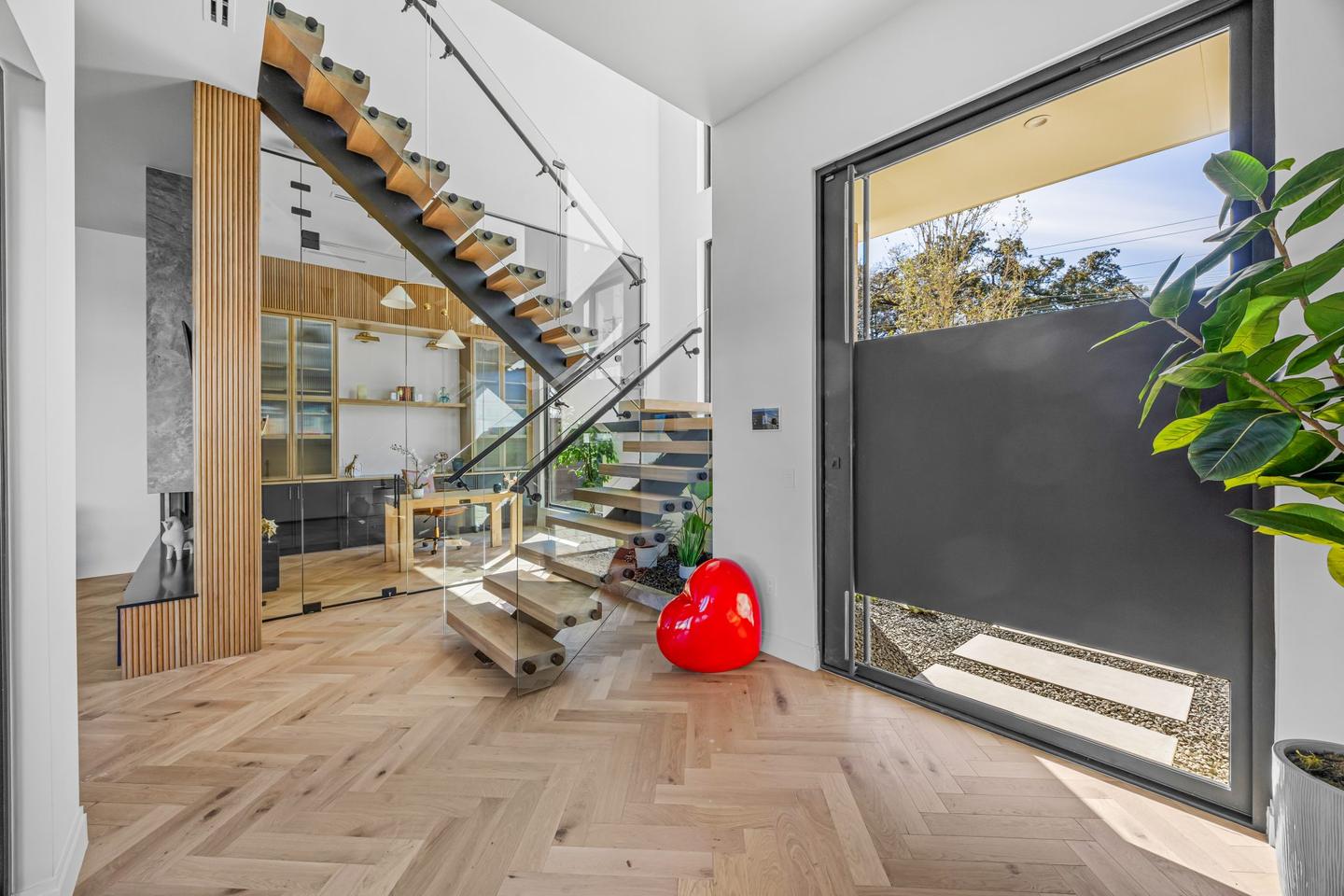 Open tread timber stair on a black steel stringer with a glazed planted courtyard behind it