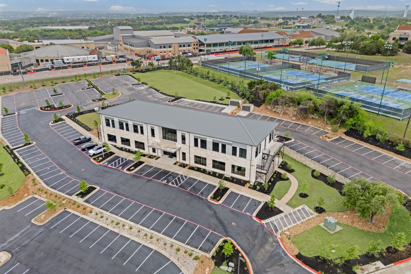 Aerial view of a two story medical office building with its parking lot, tennis courts and Lakeway beyond