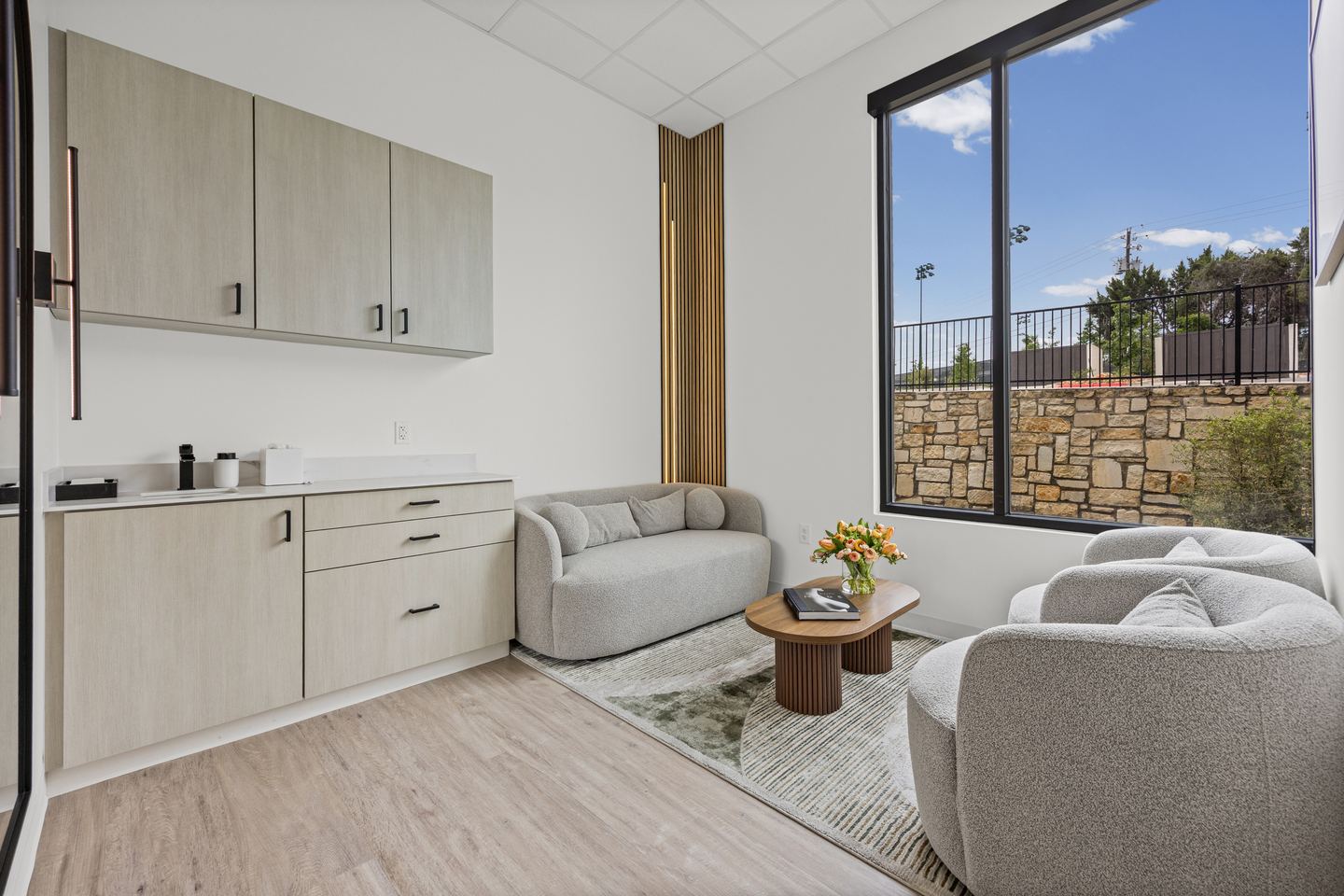 Consult room with curved cream seating, a wooden coffee table and a view out to a stone wall