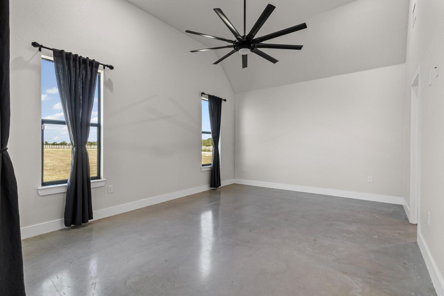 The same primary bedroom empty, with a vaulted ceiling and a large ceiling fan