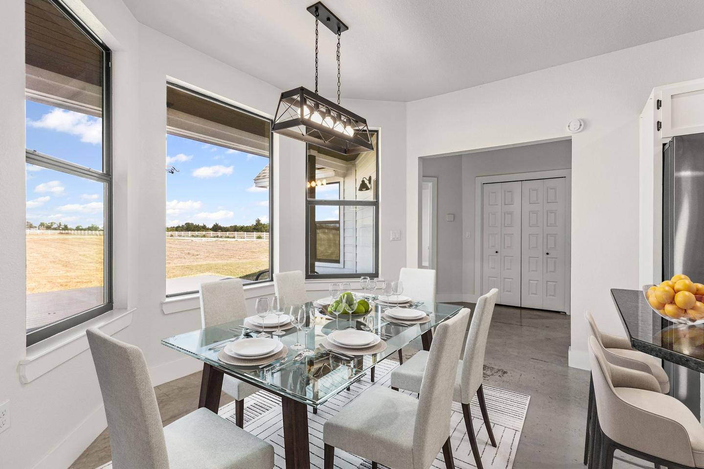 Dining area staged with a glass table and white upholstered chairs under a linear pendant