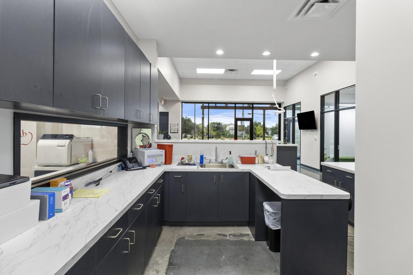 Clinical treatment room with dark cabinetry, a stainless worktop and glazing along one wall