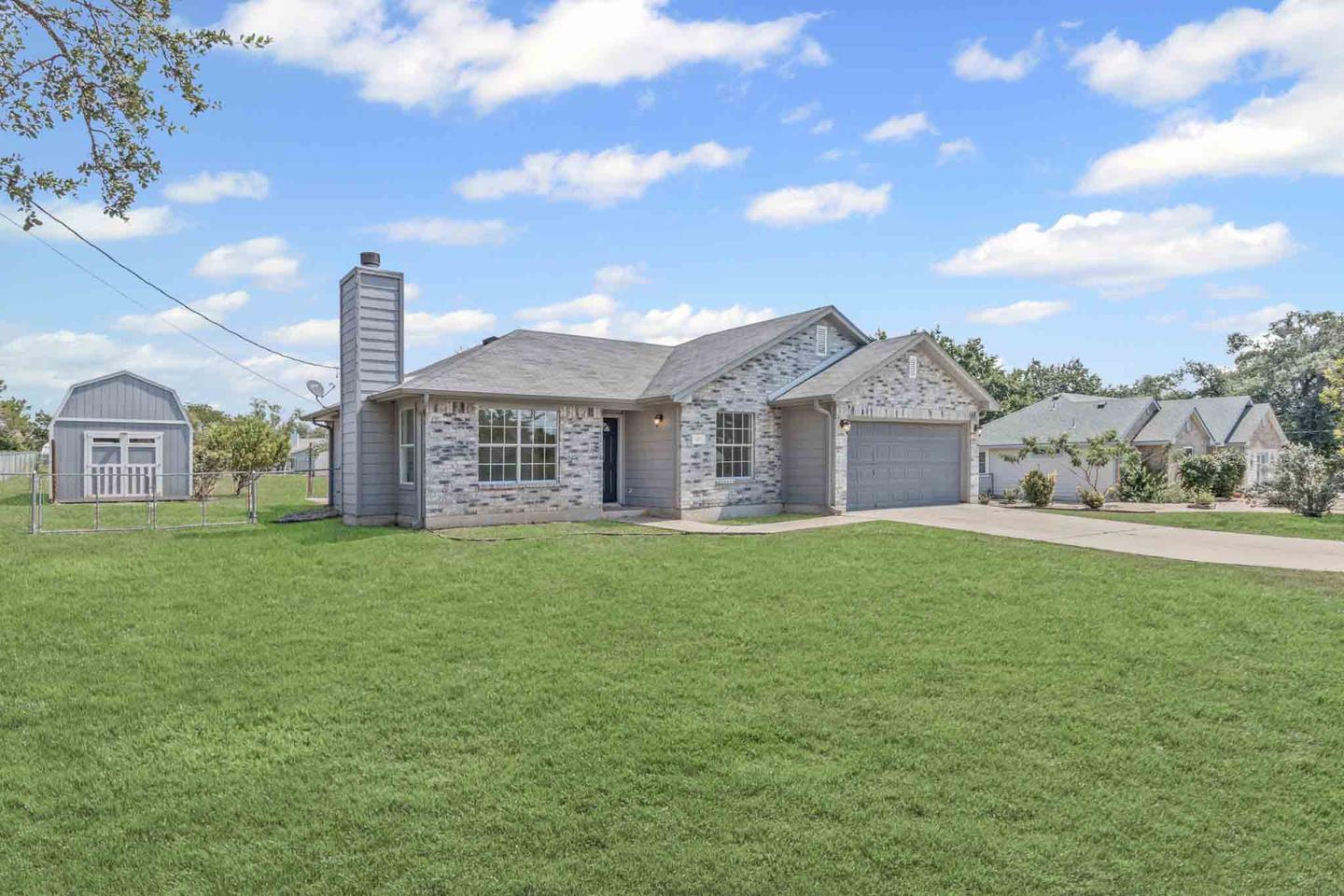 Stone home photographed across a large front lawn framed by a mature oak