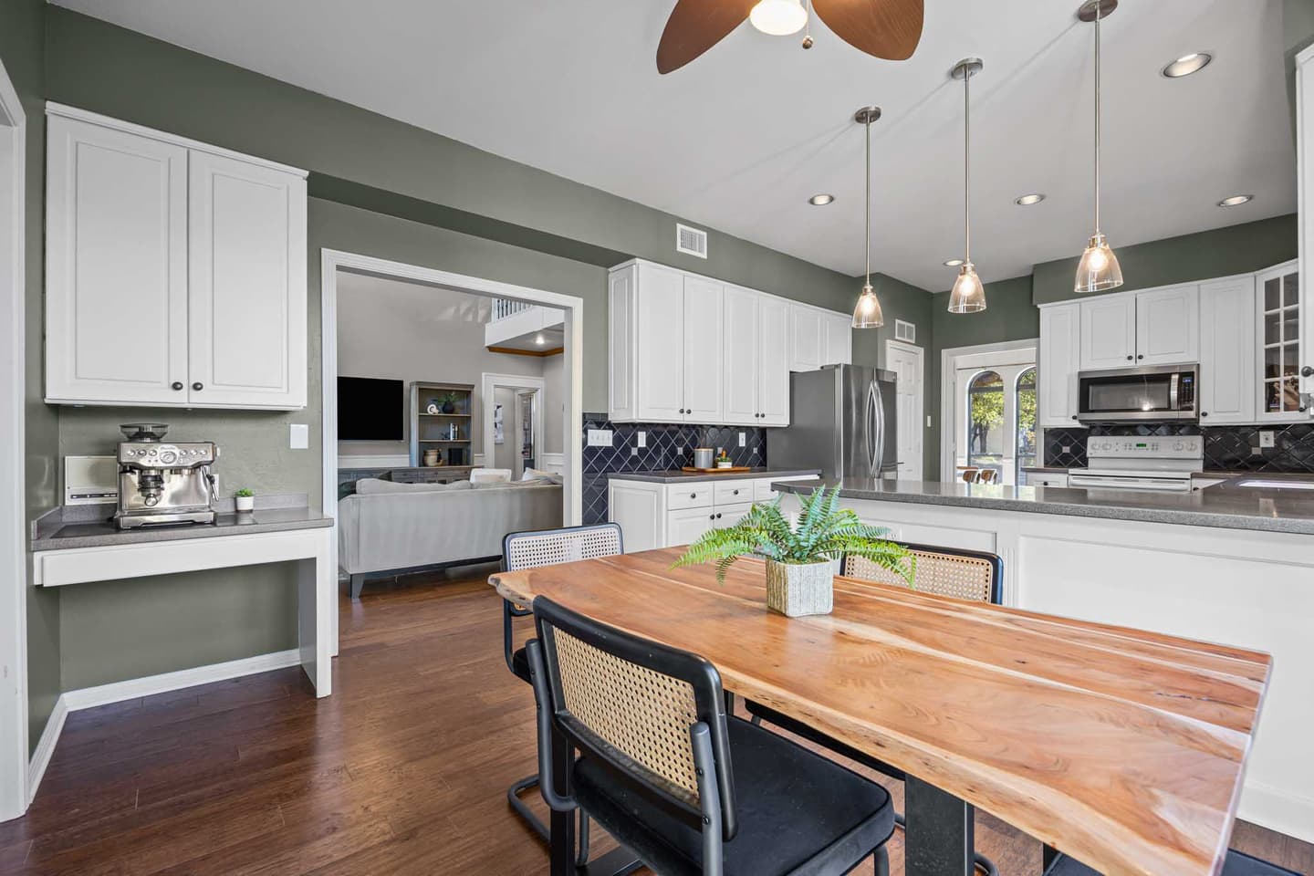Kitchen and breakfast area in West Austin with sage green walls, white cabinetry and a live edge table
