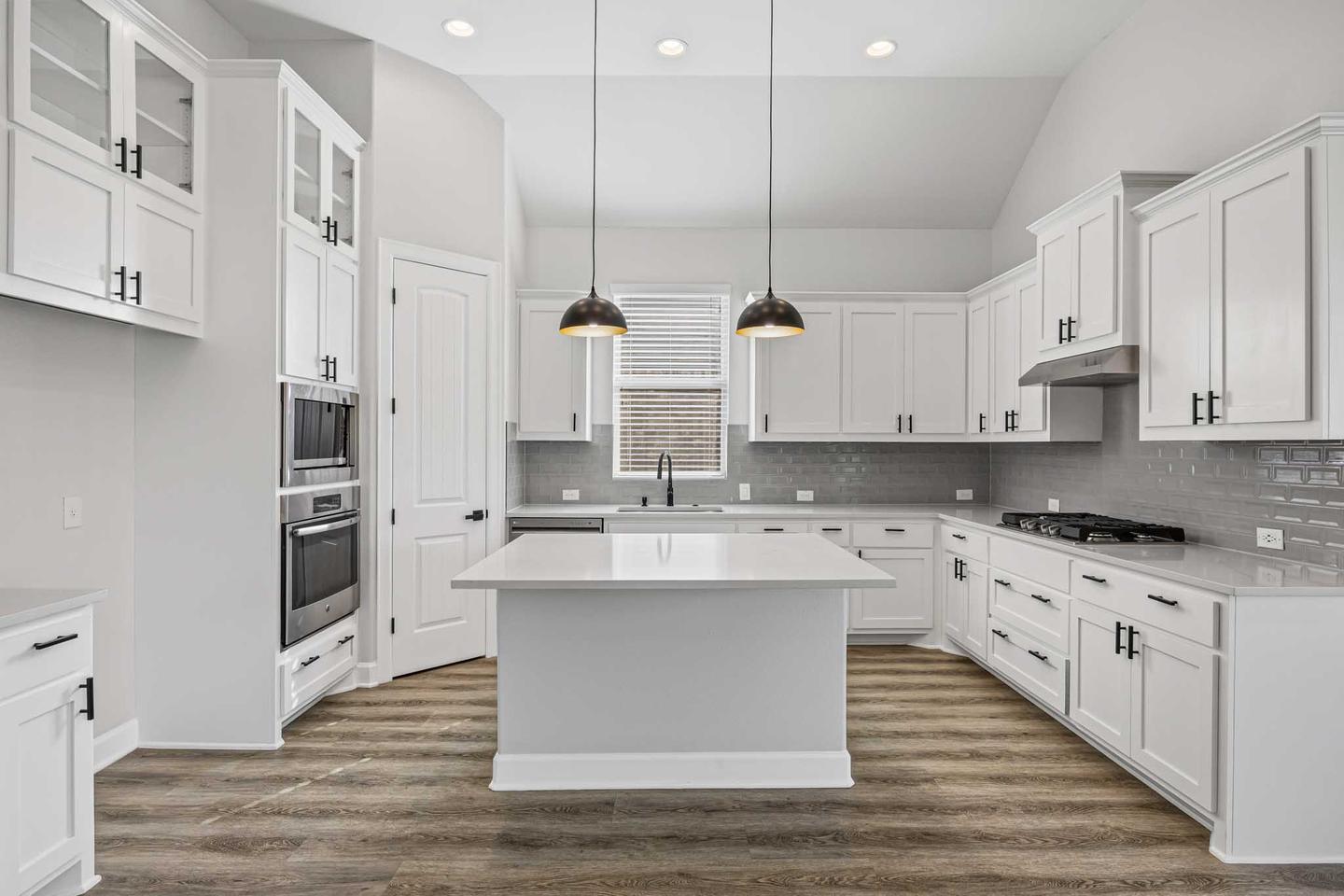 Kitchen in a Dripping Springs home with white cabinetry, a long island and pendant lights