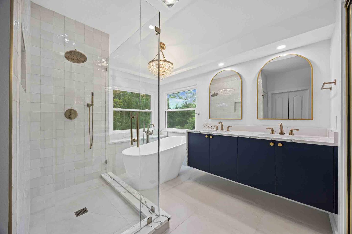 Primary bathroom with a navy double vanity, gold fixtures and a glass walk in shower