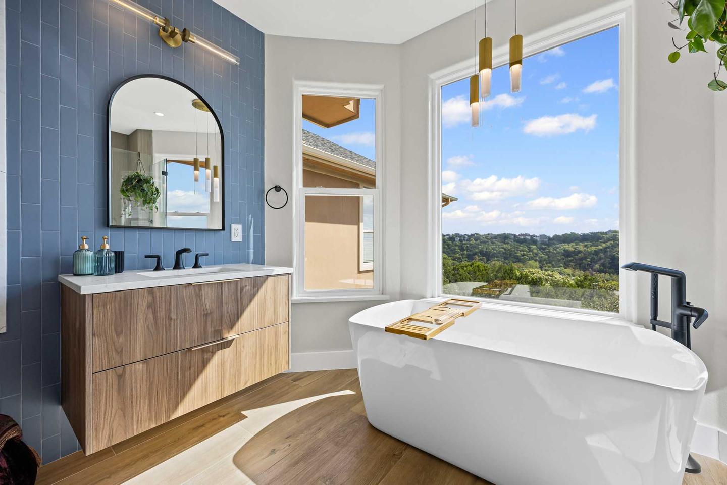 Primary bathroom in Westlake with blue tile, a floating walnut vanity and a freestanding tub beside a hill country window