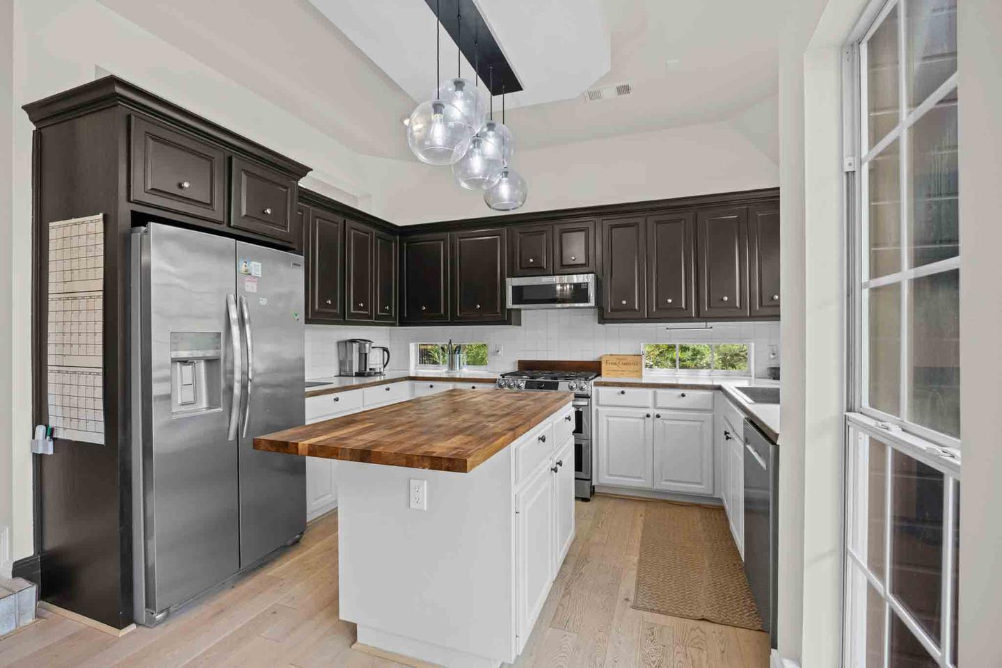 Two tone kitchen with dark cabinetry, a butcher block island and pendant lighting