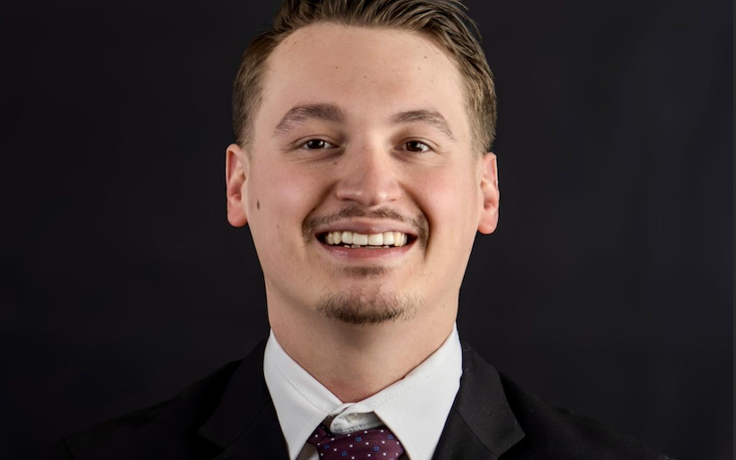 Headshot of a real estate agent in a dark suit against a plain backdrop
