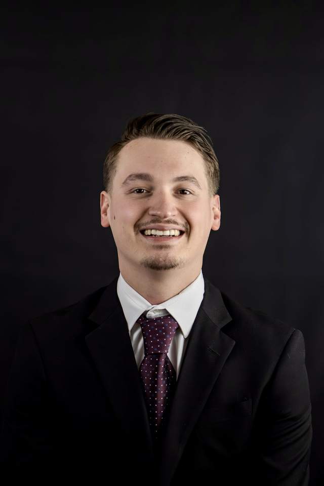 Agent headshot photographed against a black background in a suit and tie, lit from one side