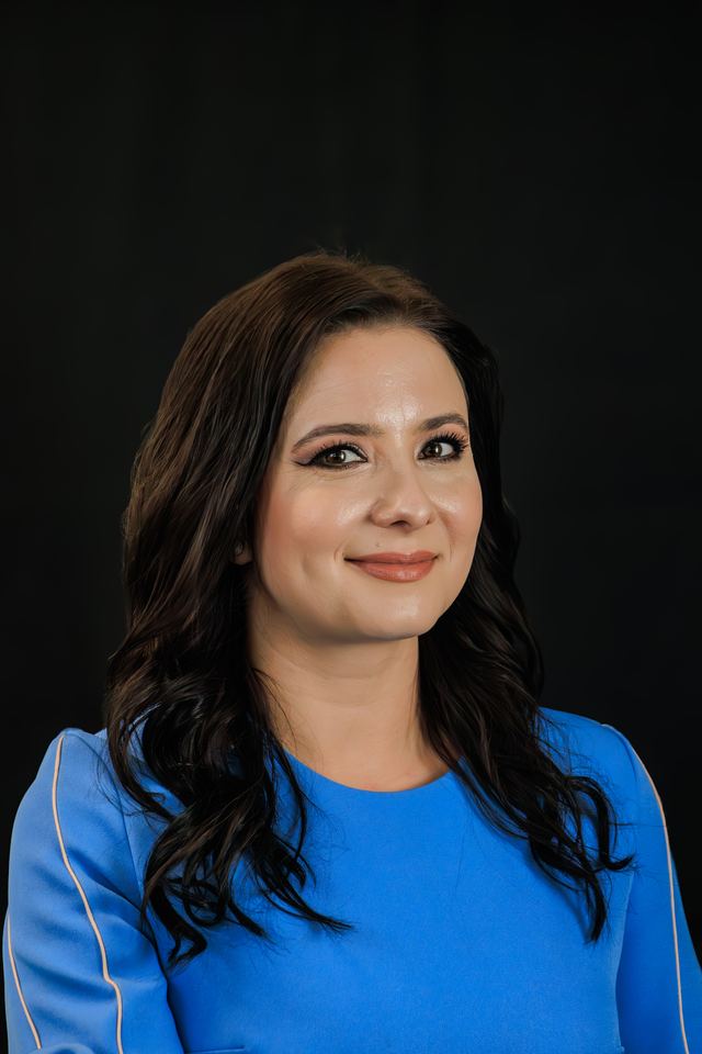 Headshot of a woman with long dark hair in a bright blue top against a black studio backdrop