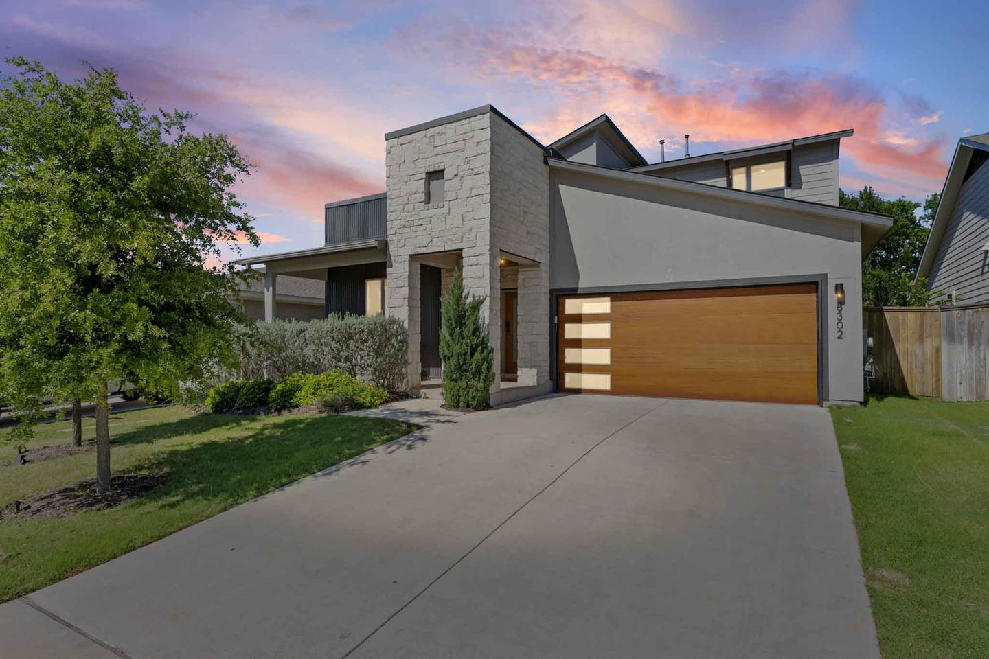 Contemporary gray home in East Austin at dusk with a wood garage door and a violet sky