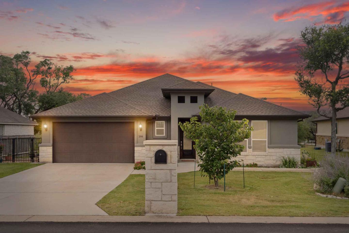 Stone single story home in Lakeway under a pink and orange dusk sky