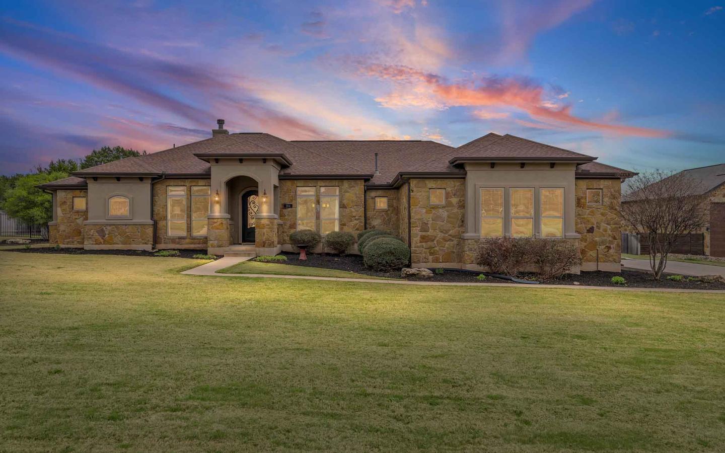 Stone fronted West Austin home at dusk with warm window light and a pink sky