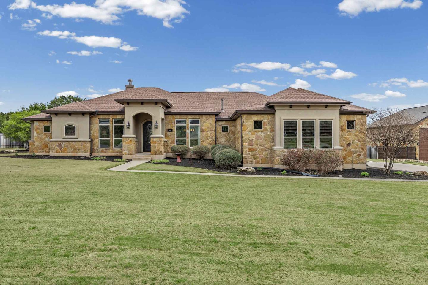 Single story stone home in West Austin photographed across a wide front lawn under a blue sky